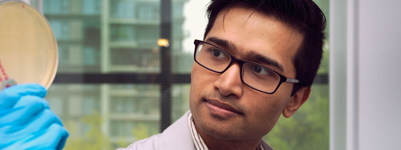 A close-up of a male pharmacist looking intently at the petri dish he is holding.