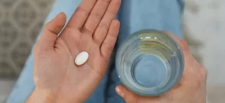A top-down image of someone holding a pill in one hand and a glass of water in the other.
