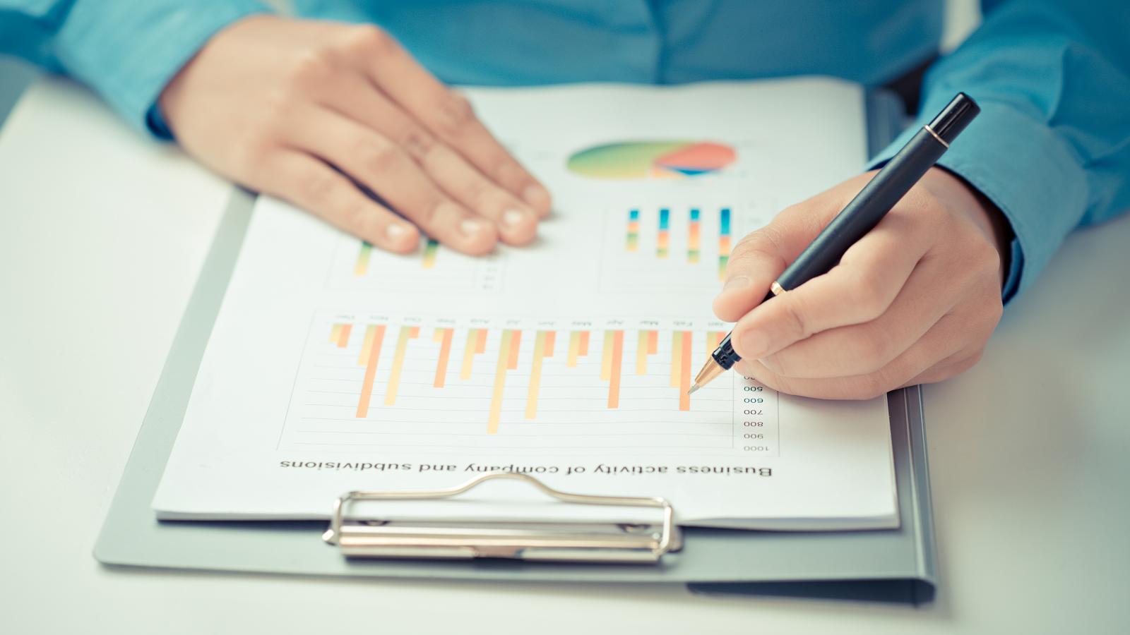 A close-up of a person writing on a clipboard page which is covered in charts.