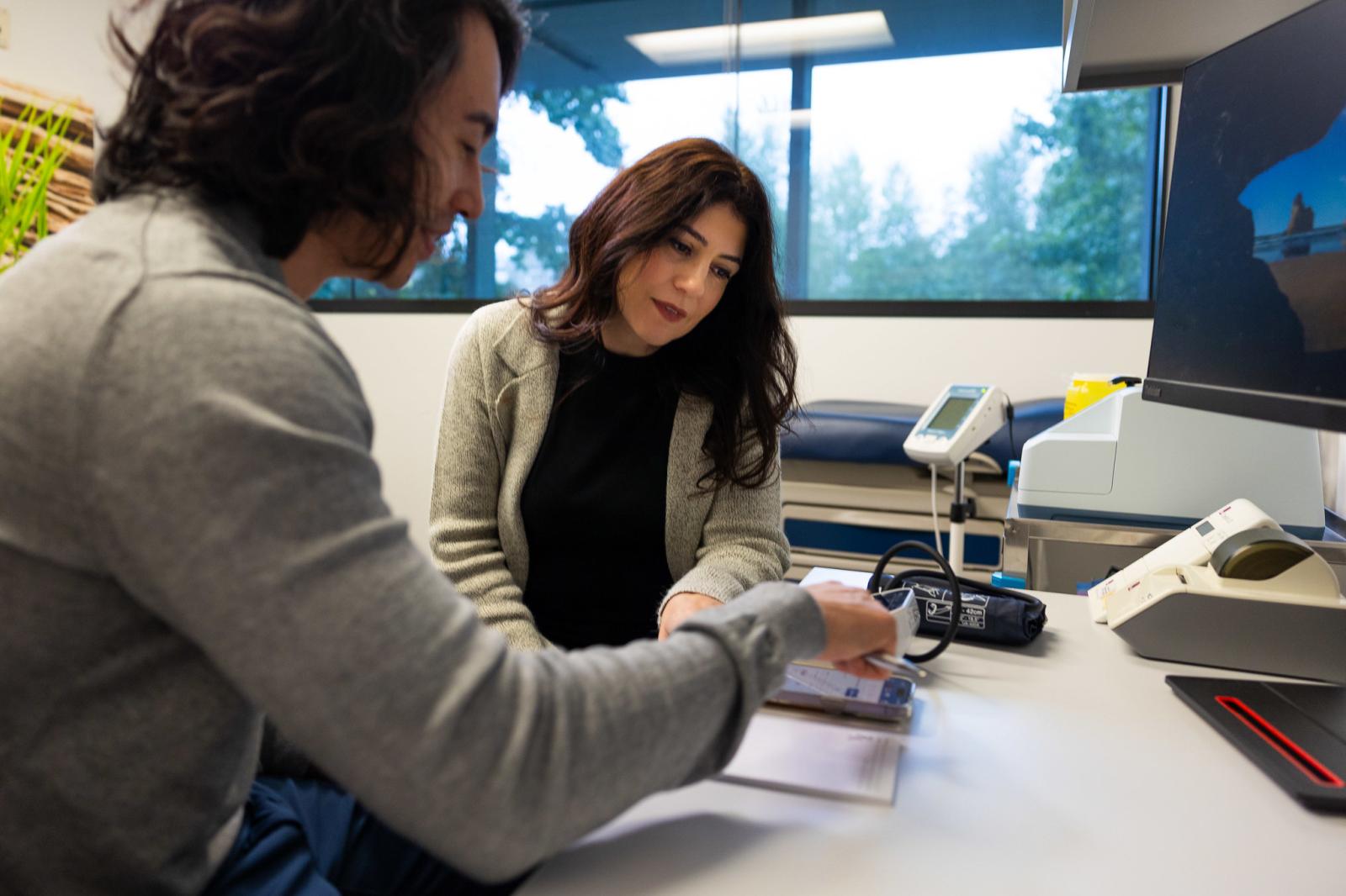 A clinic office where a pharmacist is gesturing and speaking to a patient.