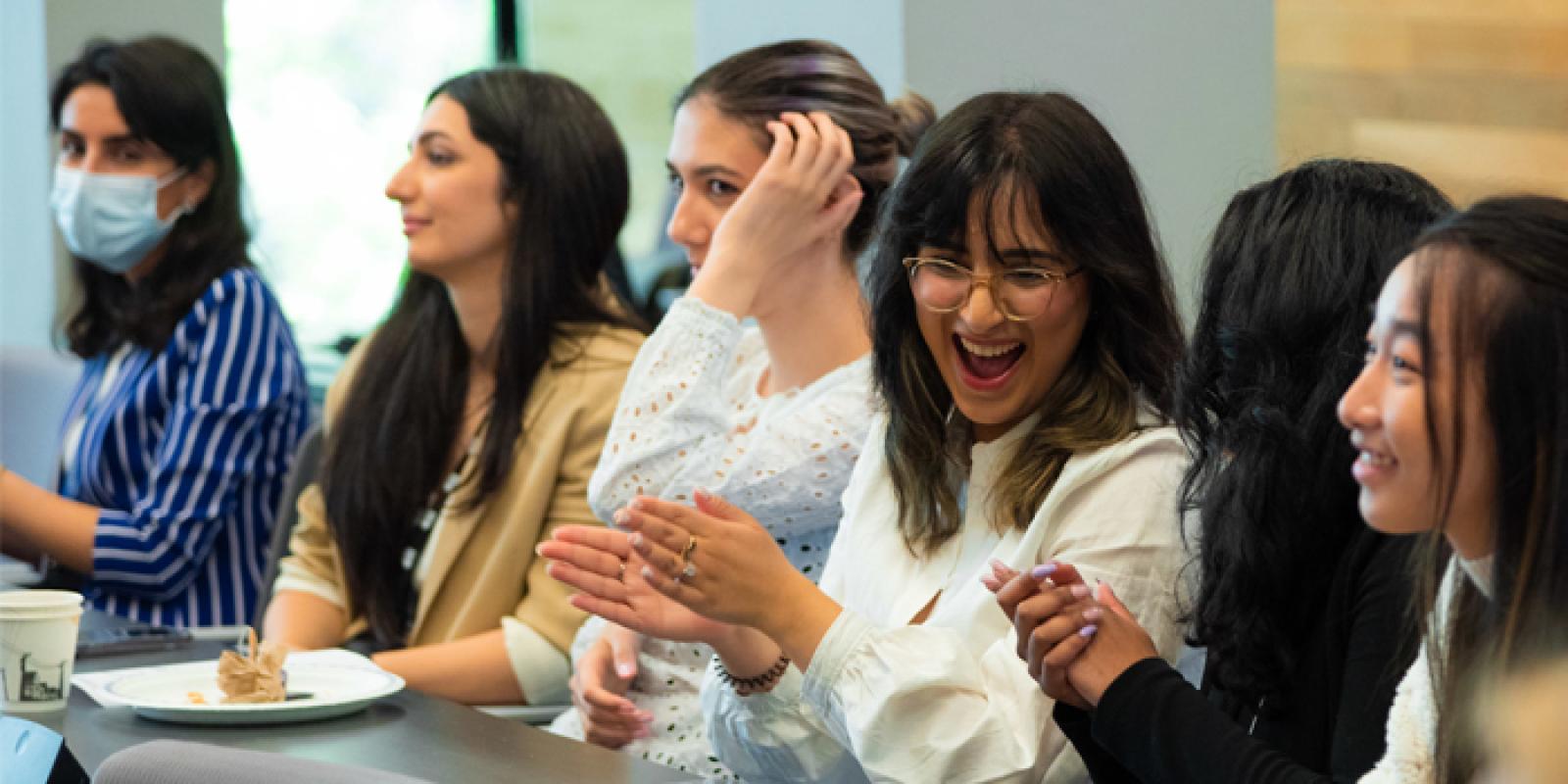 Six people sitting at a long table during a presentation;  they are smiling and clapping.