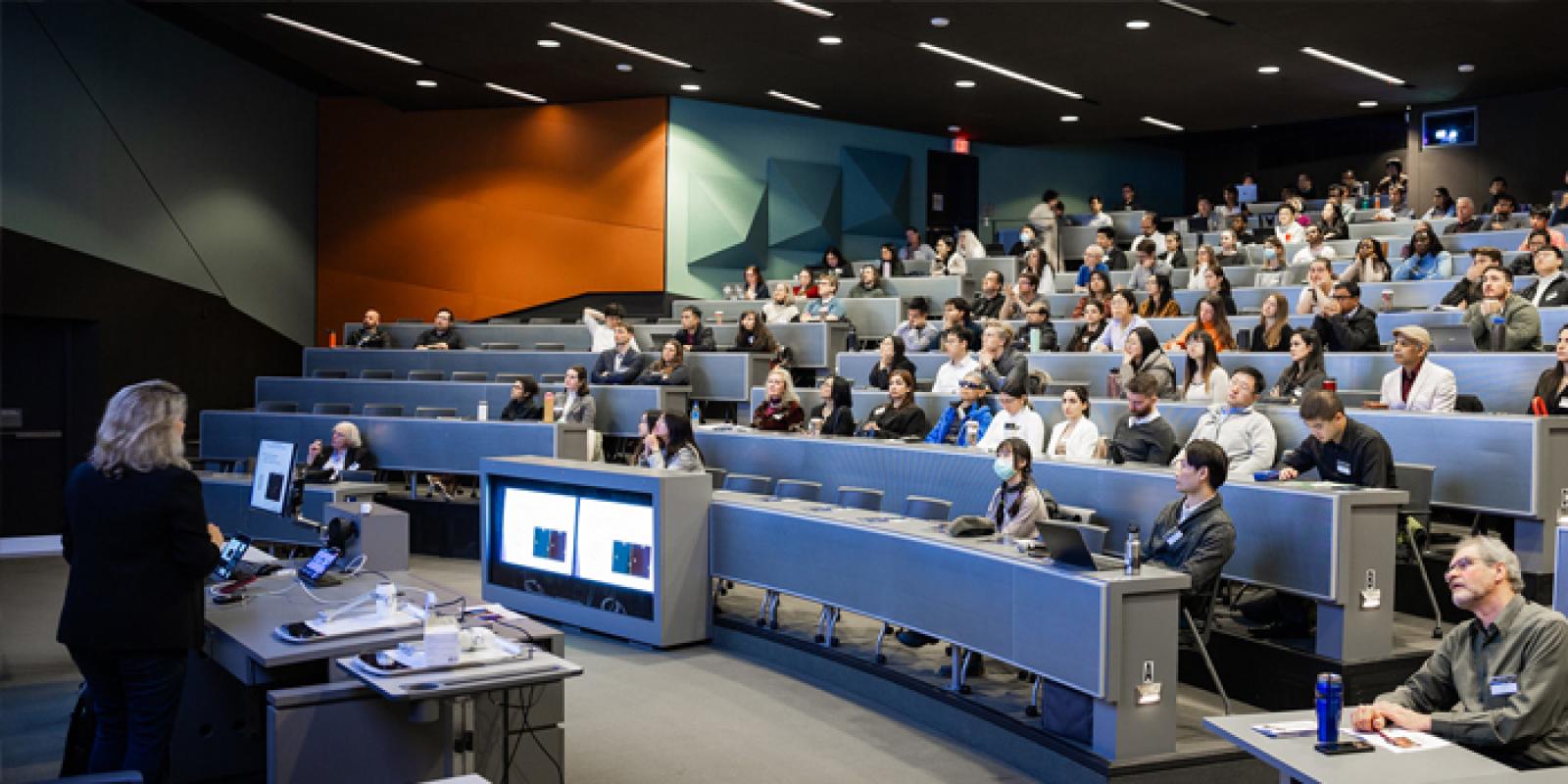 A large audience listening to a speaker in a lecture theatre.