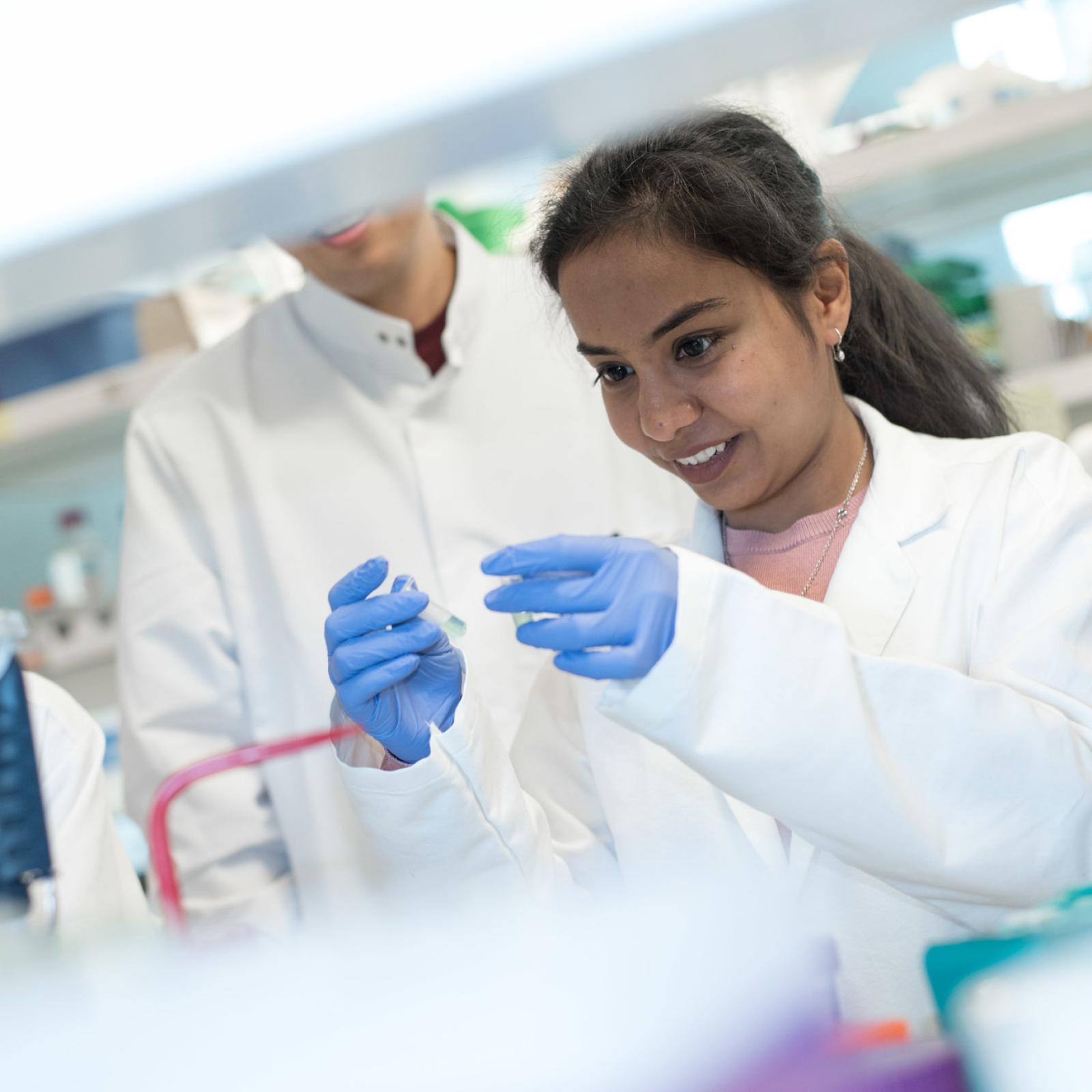 Two students in a lab; the student in the foreground is concentrating on the two test tubes she is holding.