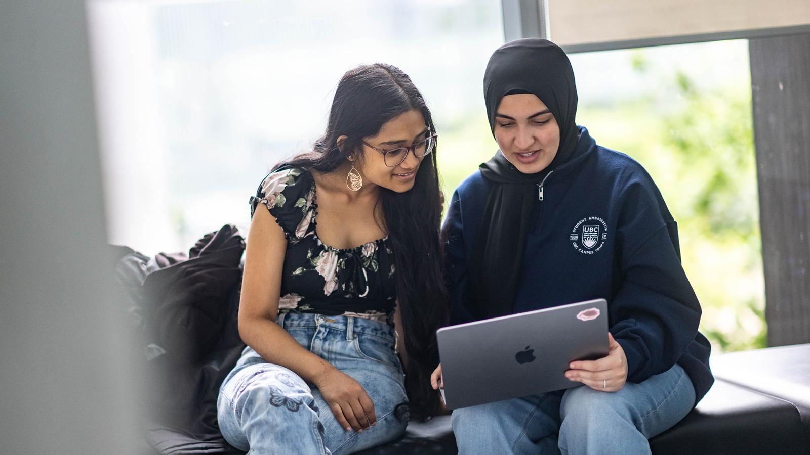 Two students sitting on a bench and looking at a laptop.